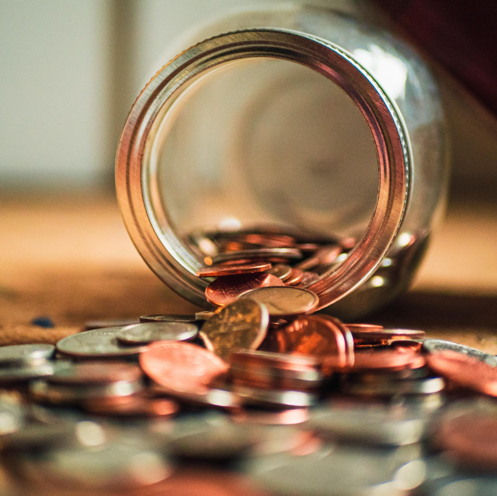 A glass jar with small change in it lies on its side as the coins spill out onto the ground.